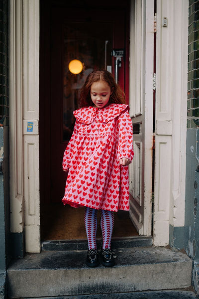 Roze Adore jurk met rode hartjesprint van Daily Brat, met rucheskraag en lange mouwen – gemaakt van biologisch katoen.