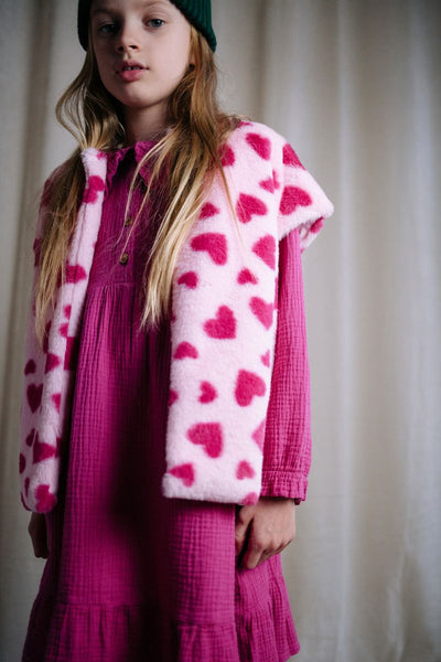 Roze teddy bodywarmer voor meisjes van Daily Brat met rode hartjesprint, mouwloos en zacht gevoerd, ideaal om over een jurk of trui te dragen.