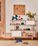 Oeuf NYC Mini Library met kinderboeken, speelgoed en een vaas met gele bloemen tegen een lichtroze muur