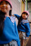 Meisje draagt de koraalroze Club Chaos beanie van Sproet & Sprout gecombineerd met een blauwe trui uit dezelfde collectie.